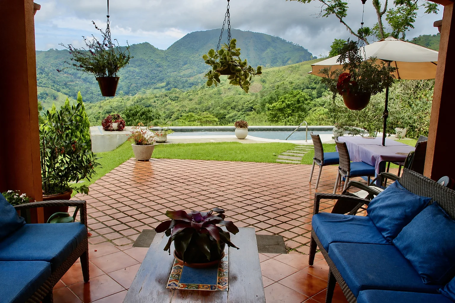 Covered terrace with blue-cushioned seating, a heated pool and sweeping green mountain views