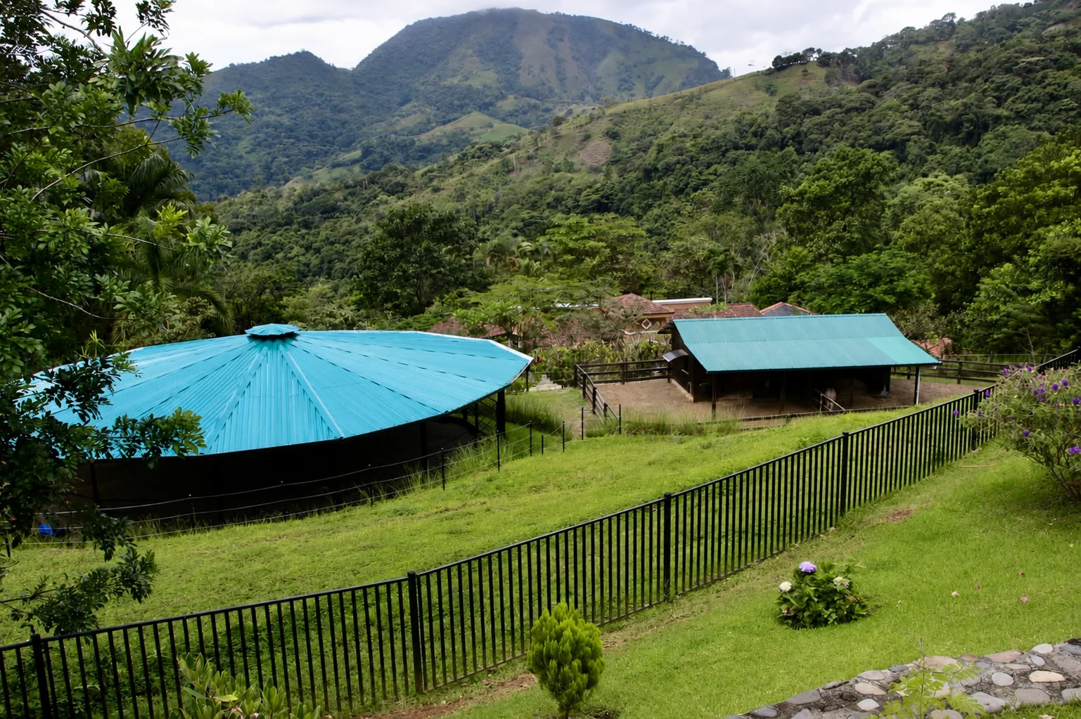Covered riding arena and stable set below the green mountains
